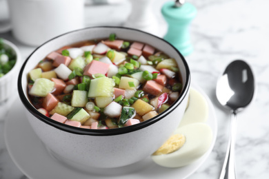 Photo of Delicious cold okroshka with kvass served on white marble table, closeup. Traditional Russian summer soup