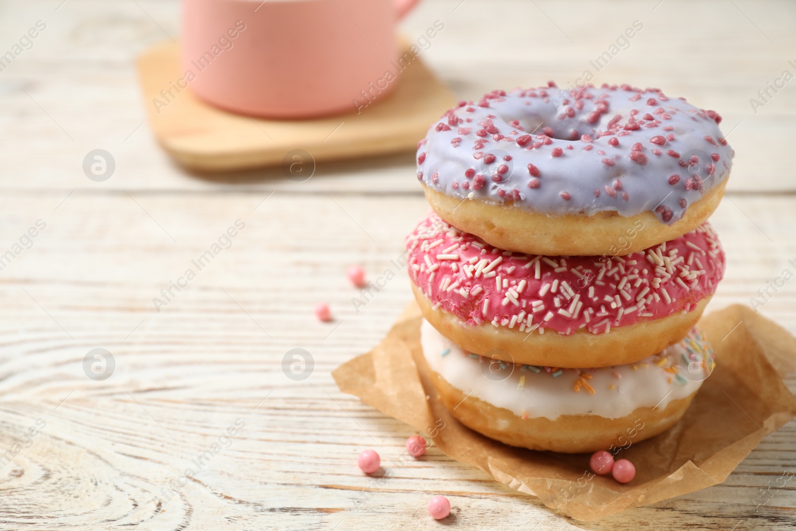 Photo of Delicious glazed donuts on white wooden table. Space for text