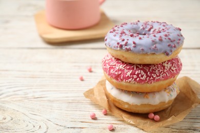 Delicious glazed donuts on white wooden table. Space for text