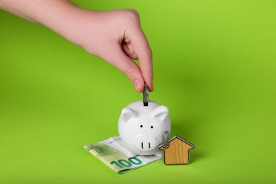 Photo of Woman putting coin into ceramic piggy bank on light green background, closeup. Financial savings