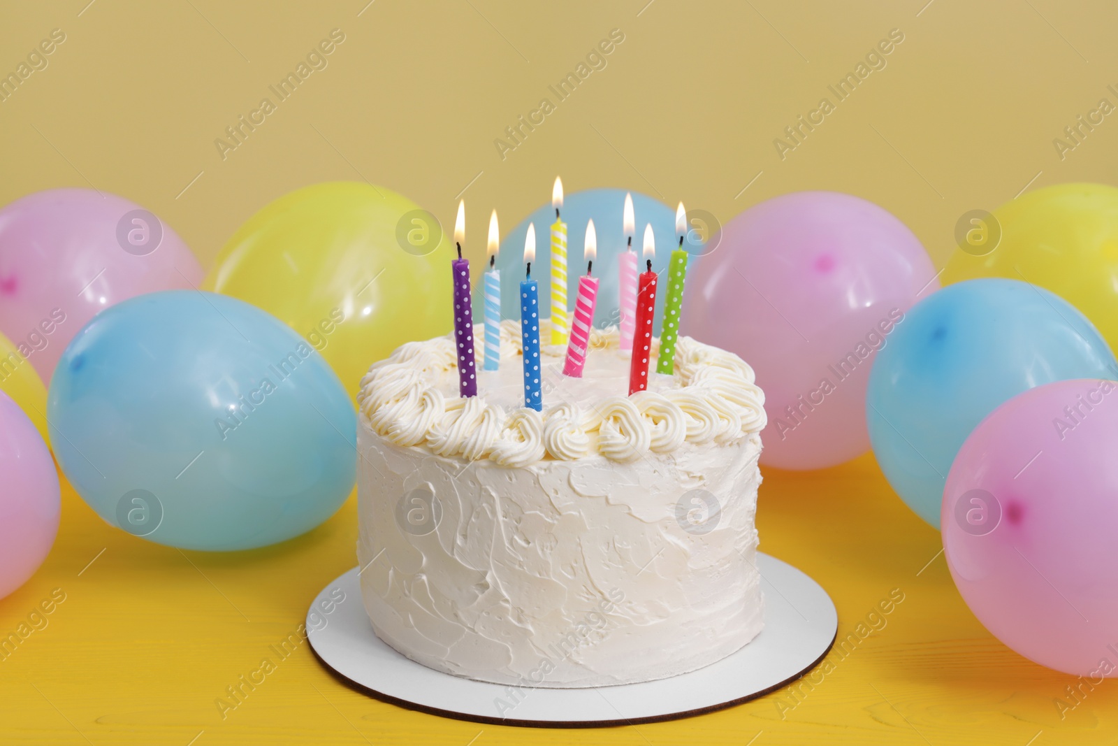 Photo of Delicious cake with burning candles and festive decor on yellow background