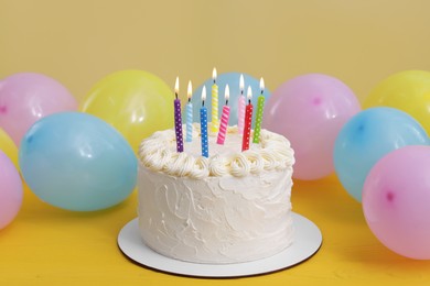 Delicious cake with burning candles and festive decor on yellow background