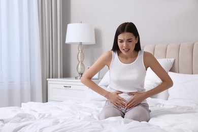 Photo of Young woman suffering from stomach ache in bedroom