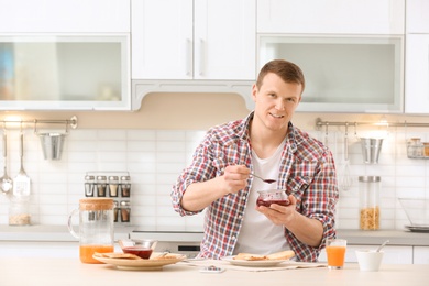 Photo of Young man with jar of jam and tasty toasted bread at table in kitchen