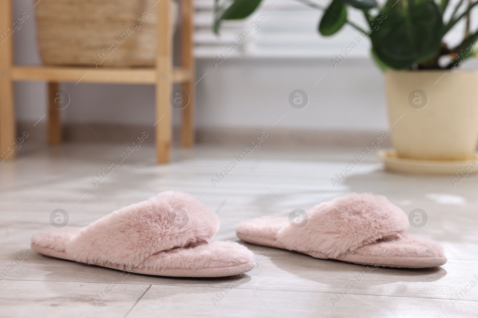 Photo of Pink soft slippers on light wooden floor at home, closeup
