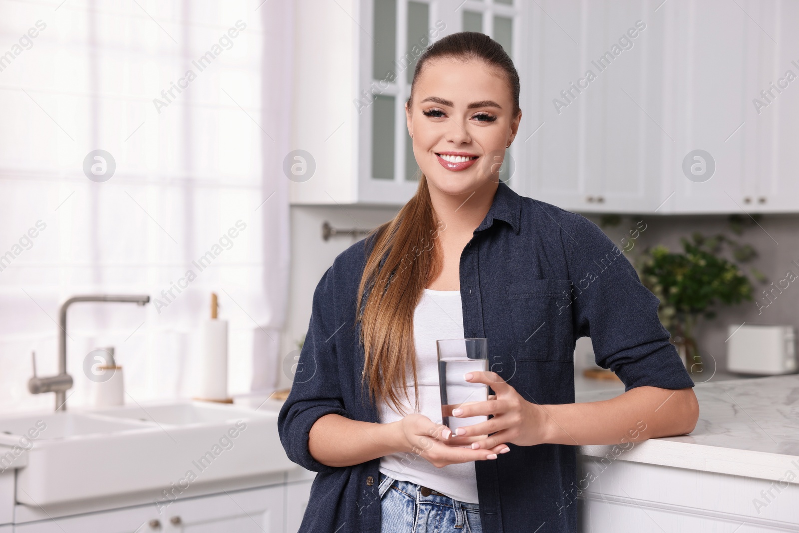 Photo of Happy woman with glass of fresh water in kitchen, space for text