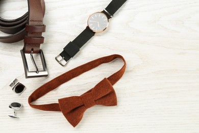 Photo of Stylish terracotta bow tie, cufflinks and wristwatch on white wooden background, flat lay. Space for text