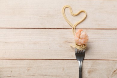 Photo of Heart made of tasty spaghetti, fork and shrimp on wooden table, top view. Space for text
