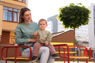 Happy nanny with cute little boy sitting on carousel outdoors, space for text