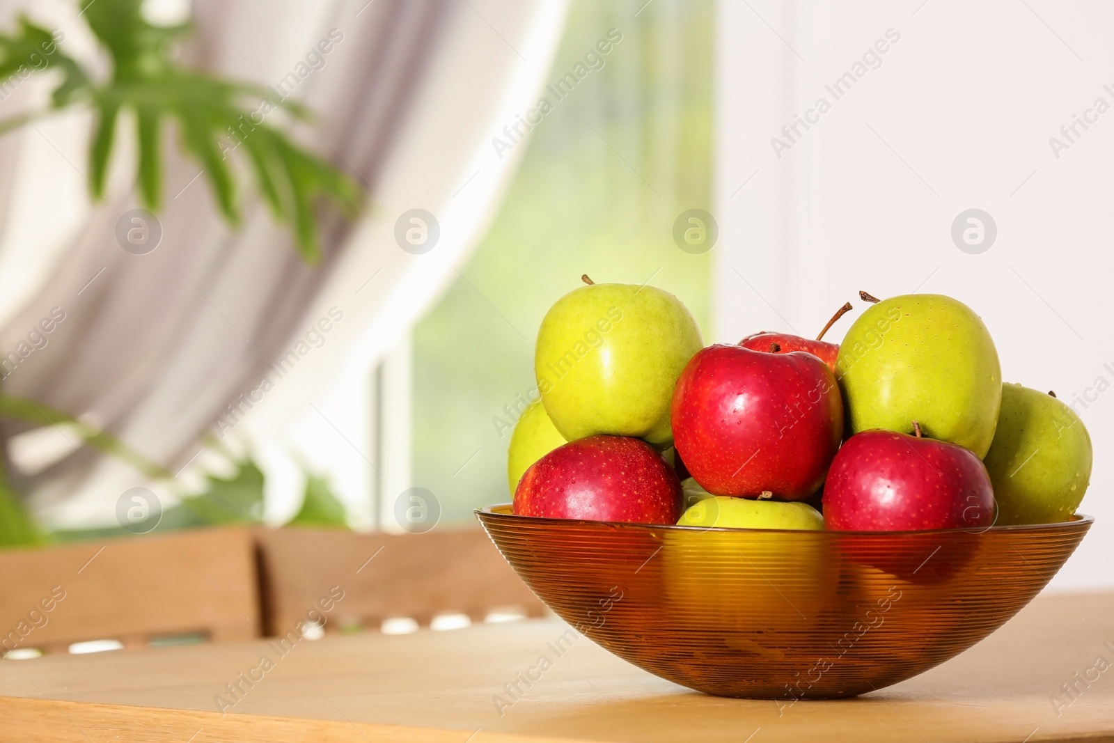 Photo of Bowl with different sweet apples on table in room, space for text