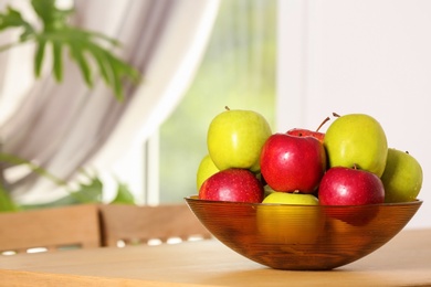 Bowl with different sweet apples on table in room, space for text