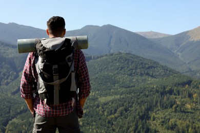 Tourist with backpack and sleeping pad in mountains on sunny day, back view