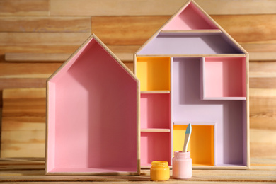 Photo of House shaped shelves, jars of paints and brush on wooden table. Interior elements