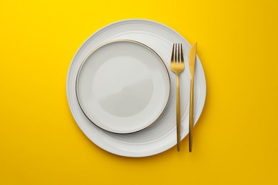 Clean plates, fork and knife on yellow background, top view