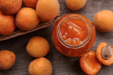 Photo of Jar of delicious jam and fresh ripe apricots on wooden table, flat lay. Fruit preserve
