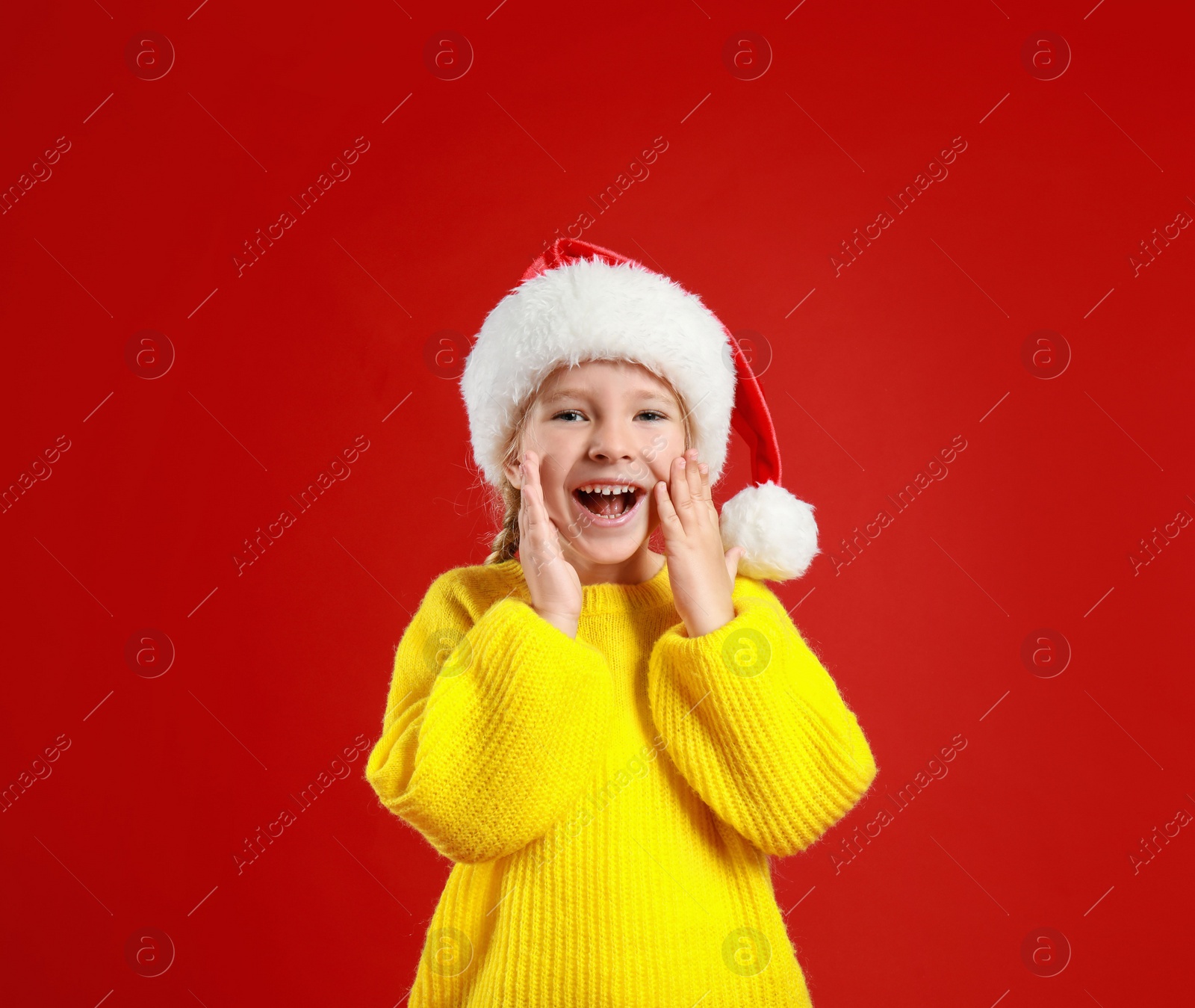 Photo of Cute little child wearing Santa hat on red background. Christmas holiday