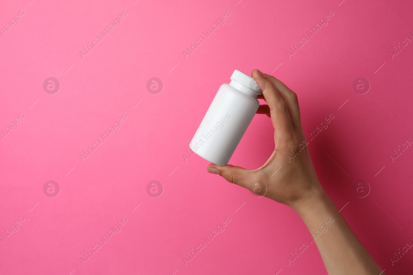 Photo of Woman holding bottle of pills on pink background, closeup. Space for text