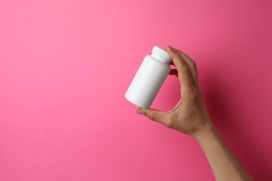 Photo of Woman holding bottle of pills on pink background, closeup. Space for text