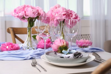 Stylish table setting with beautiful peonies, napkin and blank card indoors