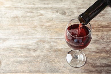 Photo of Pouring delicious red wine into glass on wooden background