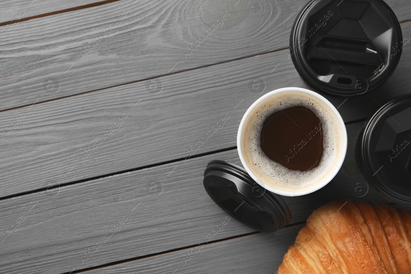 Photo of Coffee to go. Paper cups with tasty drink and croissant on grey wooden table, flat lay. Space for text