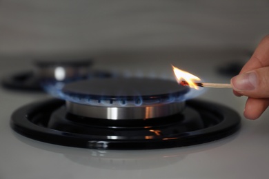 Photo of Woman lighting gas stove with match, closeup