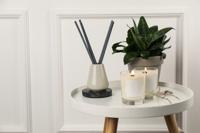 Photo of Burning soy candles, freshener and houseplant on white wooden table indoors. Space for text