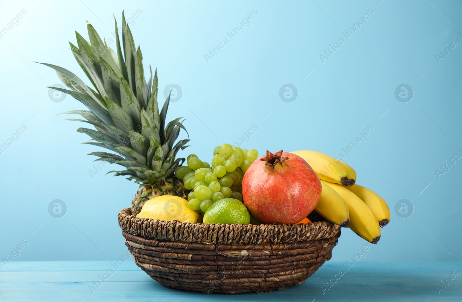 Photo of Wicker bowl with different ripe fruits on turquoise wooden table