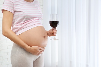 Photo of Pregnant woman with glass of red wine indoors, space for text. Alcohol addiction