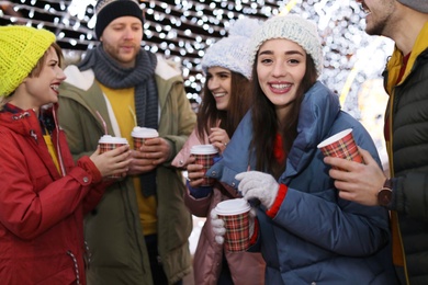 Photo of Happy friends with cups of mulled wine at winter fair