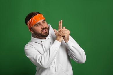 Fashionable young man in stylish outfit with bandana on green background