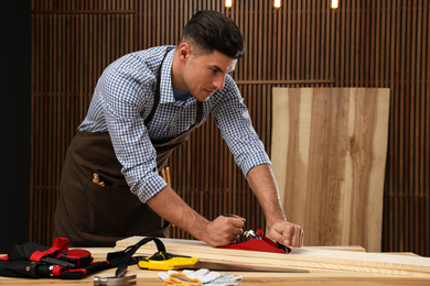Photo of Handsome carpenter working with timber at table indoors