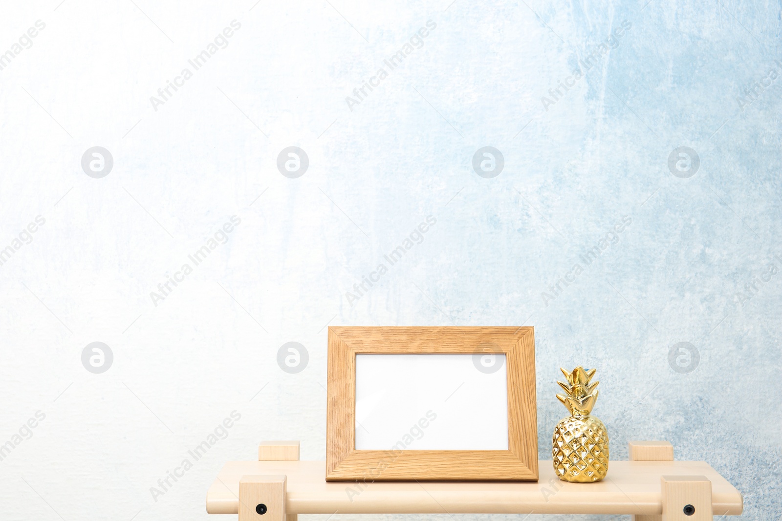 Photo of Blank frame and decorative pineapple figure on table near light wall. Mock up for design