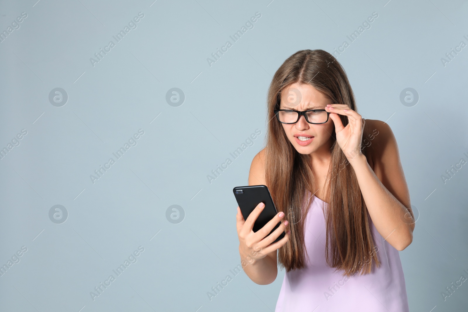 Photo of Young woman with vision problems using smartphone on grey background, space for text