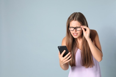 Photo of Young woman with vision problems using smartphone on grey background, space for text