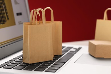 Photo of Mini shopping bags on laptop against red background, closeup. Online store