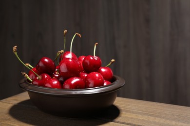 Photo of Sweet red cherries in bowl on wooden table, space for text