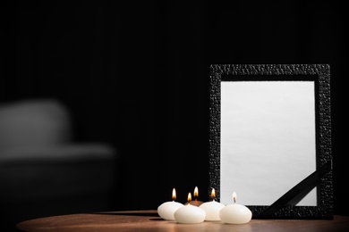 Photo of Funeral photo frame with black ribbon and candles on wooden table indoors. Space for design