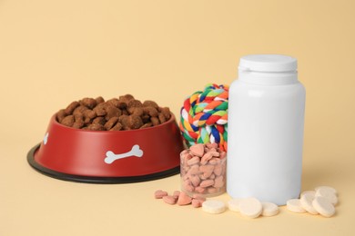 Photo of Vitamins, toy and dry pet food in bowl on beige background