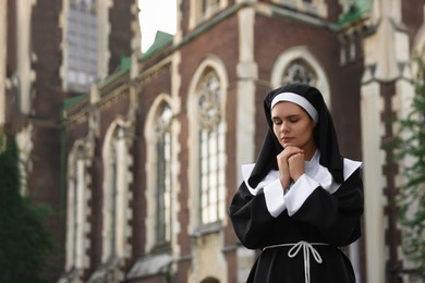 Young nun with hands clasped together while praying near cathedral outdoors, space for text