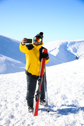 Photo of Young man with ski taking selfie on hill. Winter vacation