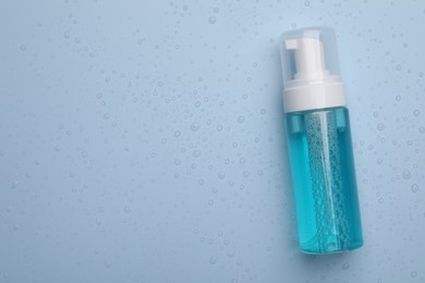 Wet bottle of face cleansing product on light blue background, top view. Space for text