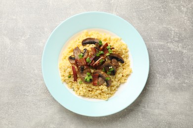 Photo of Tasty millet porridge with mushrooms, bacon and green onion on grey textured table, top view