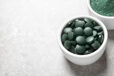 Photo of Bowls of spirulina pills and powder on color background, space for text