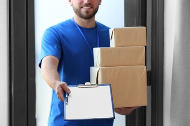 Young courier with parcels and clipboard indoors, closeup