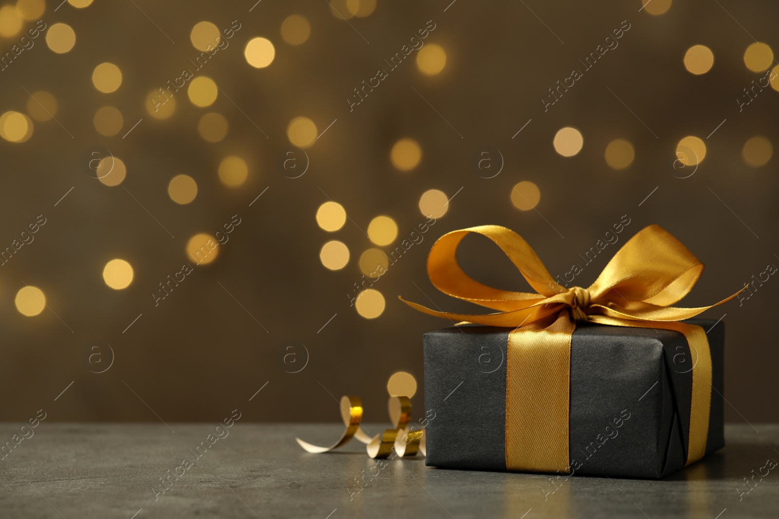 Photo of Beautifully wrapped gift box on grey table against blurred festive lights, space for text