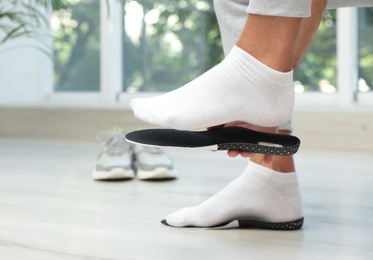 Photo of Man fitting orthopedic insole indoors, closeup. Foot care