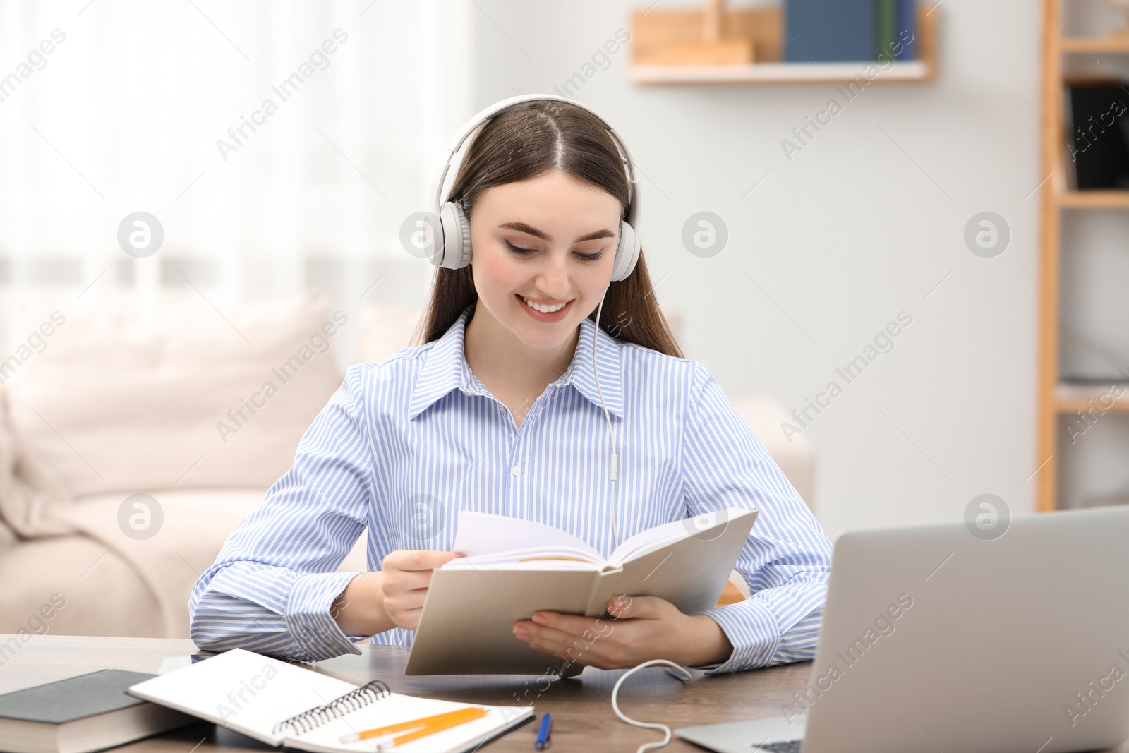 Photo of E-learning. Young woman with book during online lesson at table indoors