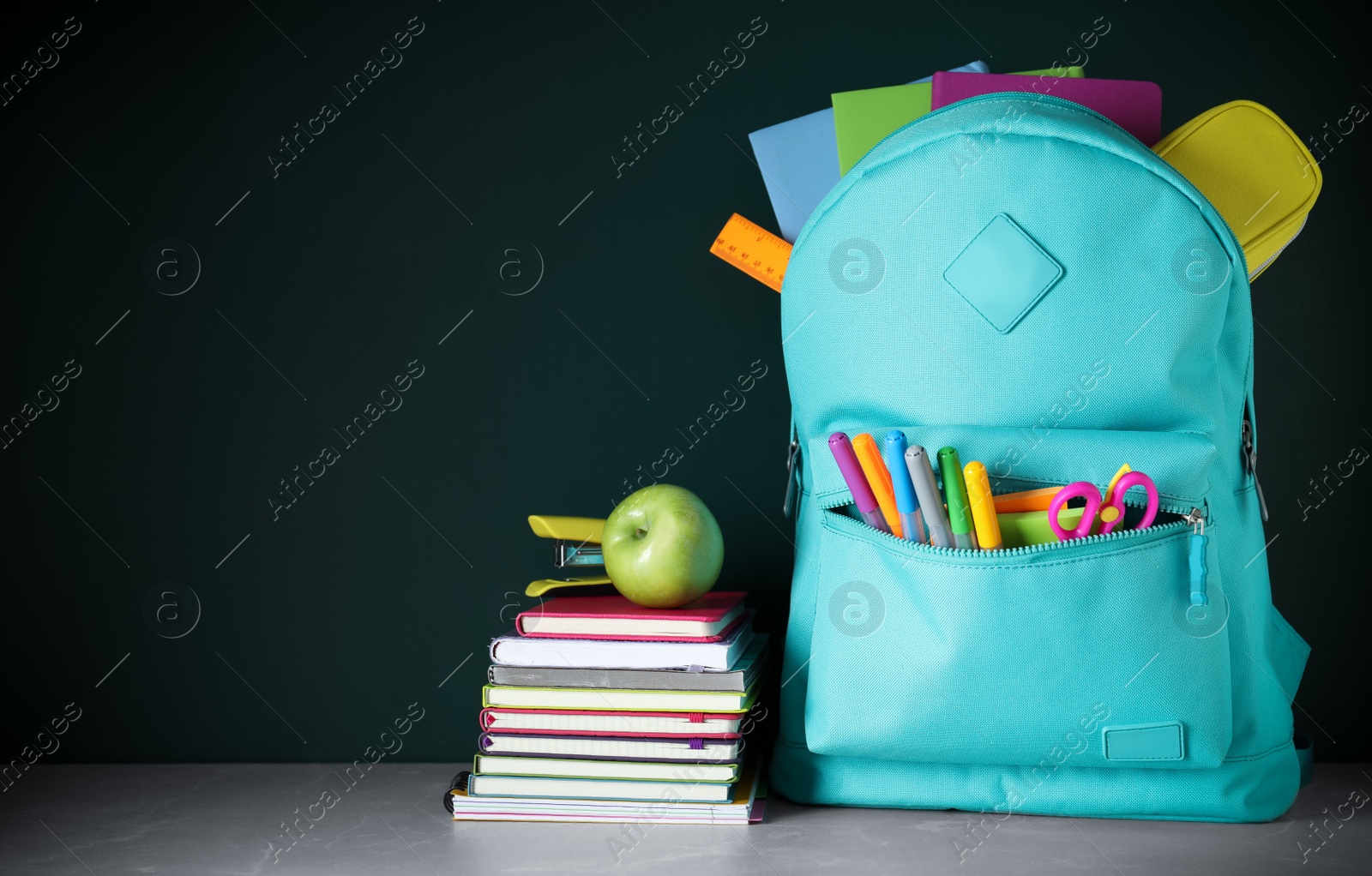 Photo of Stylish backpack with different school stationery on table against chalkboard. Space for text