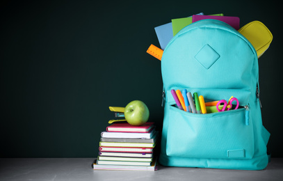 Stylish backpack with different school stationery on table against chalkboard. Space for text